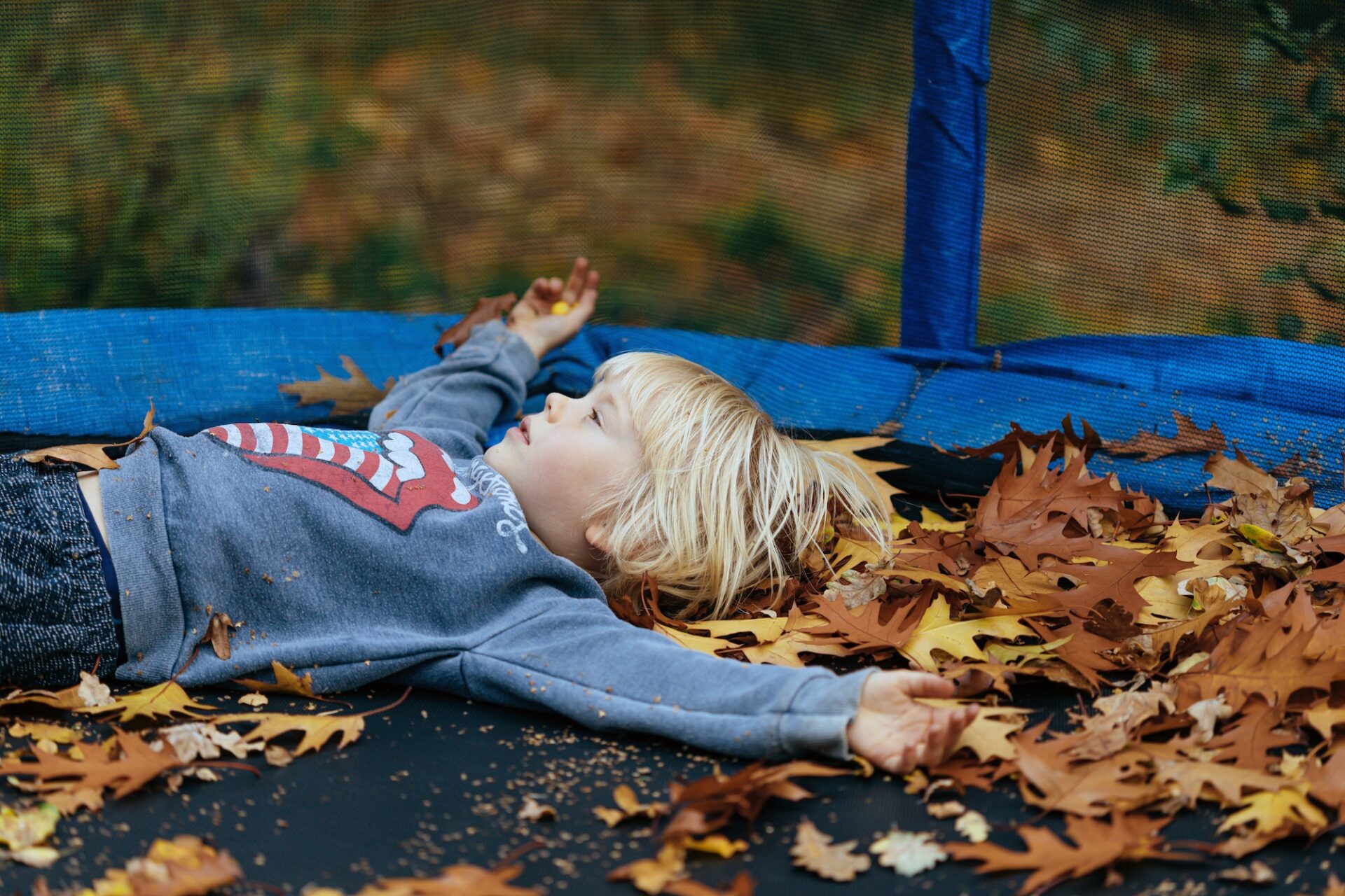 the boy lies on a trampoline among the leaves